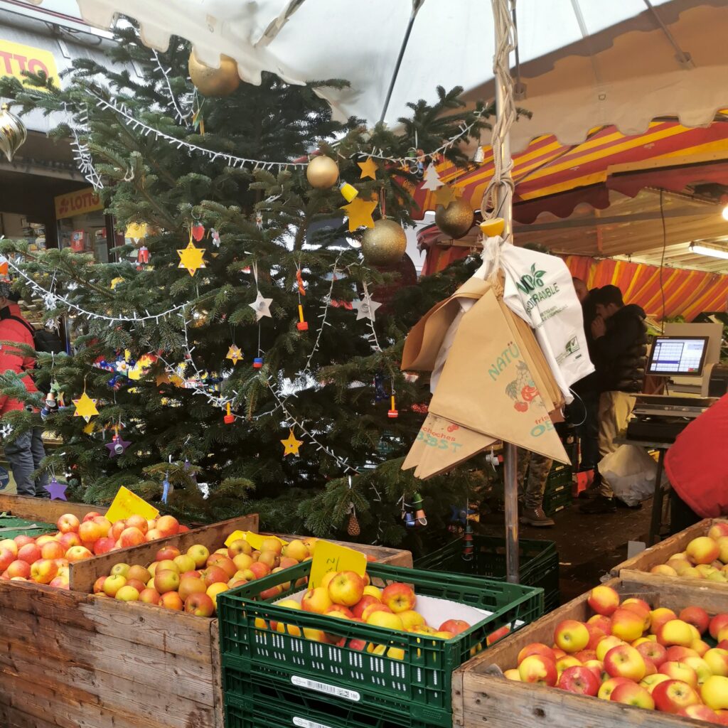 Marktstand mit Äpfeln, im Hintergrund ein geschmückter Weihnachtsbaum 