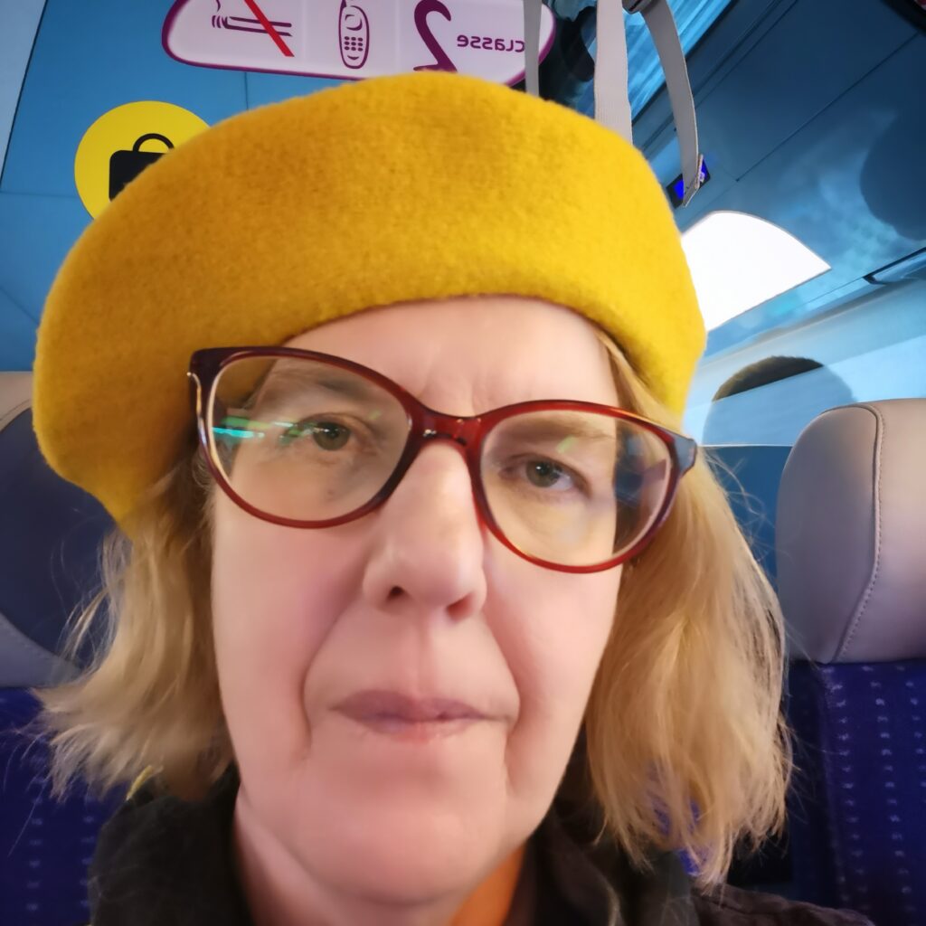 Bildbeschreibung: Selfie von Claudia mit gelbem Barret und roter Brille im Zug